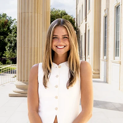 Caroline Kunkel, standing on the portico of Sadler Hall