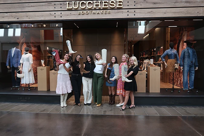 Three interns, including Cate, hold up boots in front of a Lucchese Bootmaker storefront