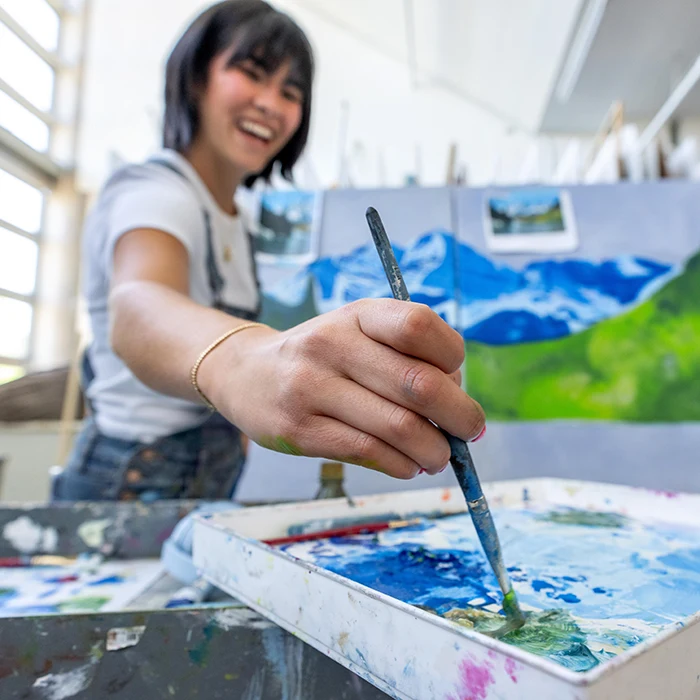 A student in the painting lab laughs while loading more paint onto her paint brush