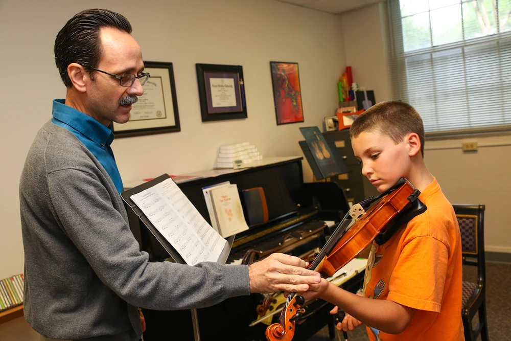 An instructor gives direction about left hand placement on a violin
