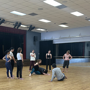 Sheaff demonstrates a dance posture low to the floor as dancers look on