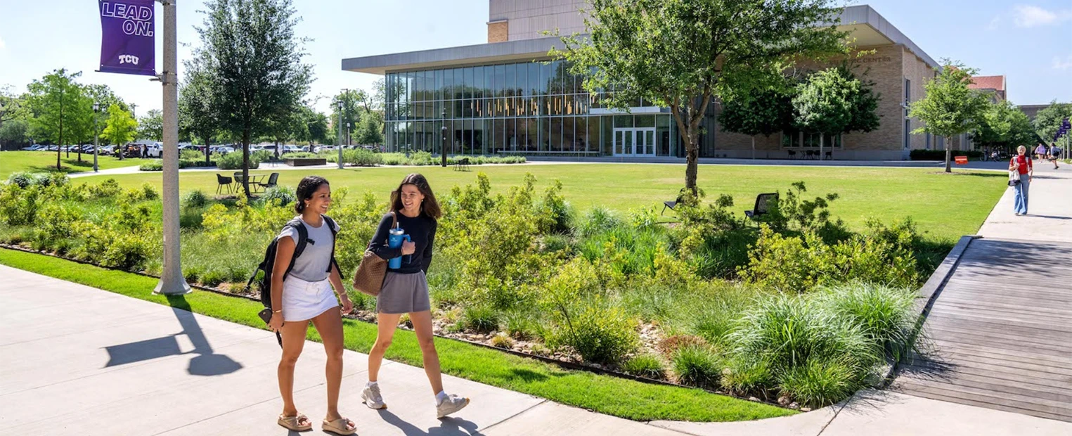 Two students chat as they walk along the Baker Martin Creative Commons, with the Boschini Music Center in the background