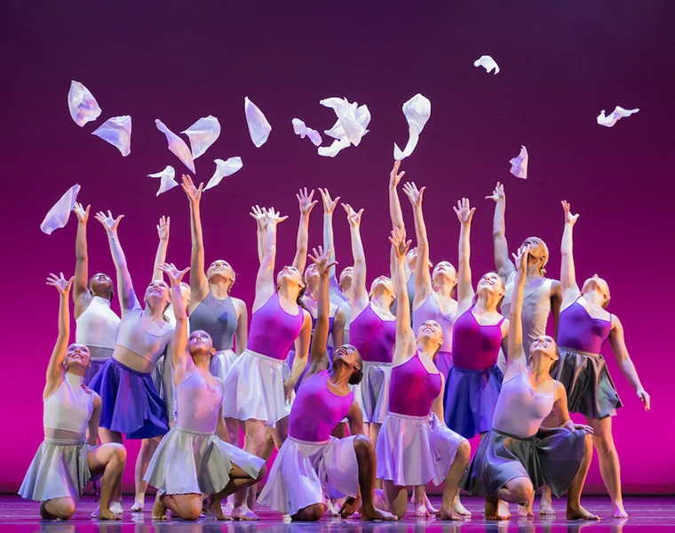 Dancers toss white handkerchiefs in the air in front of a pink backdrop