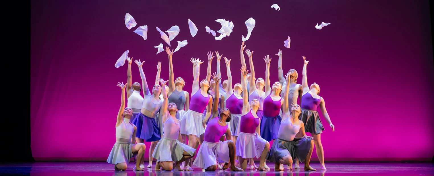 Dancers toss white handkerchiefs in the air in front of a pink backdrop