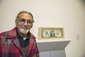 Enrique Chagoya, in a red plaid jacket, stands in front of one of his exhibit pieces