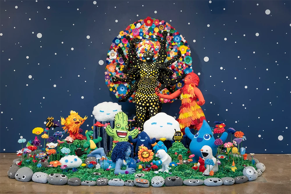 An installation of soft sculpture stands in front of a wall painted like a starry night sky