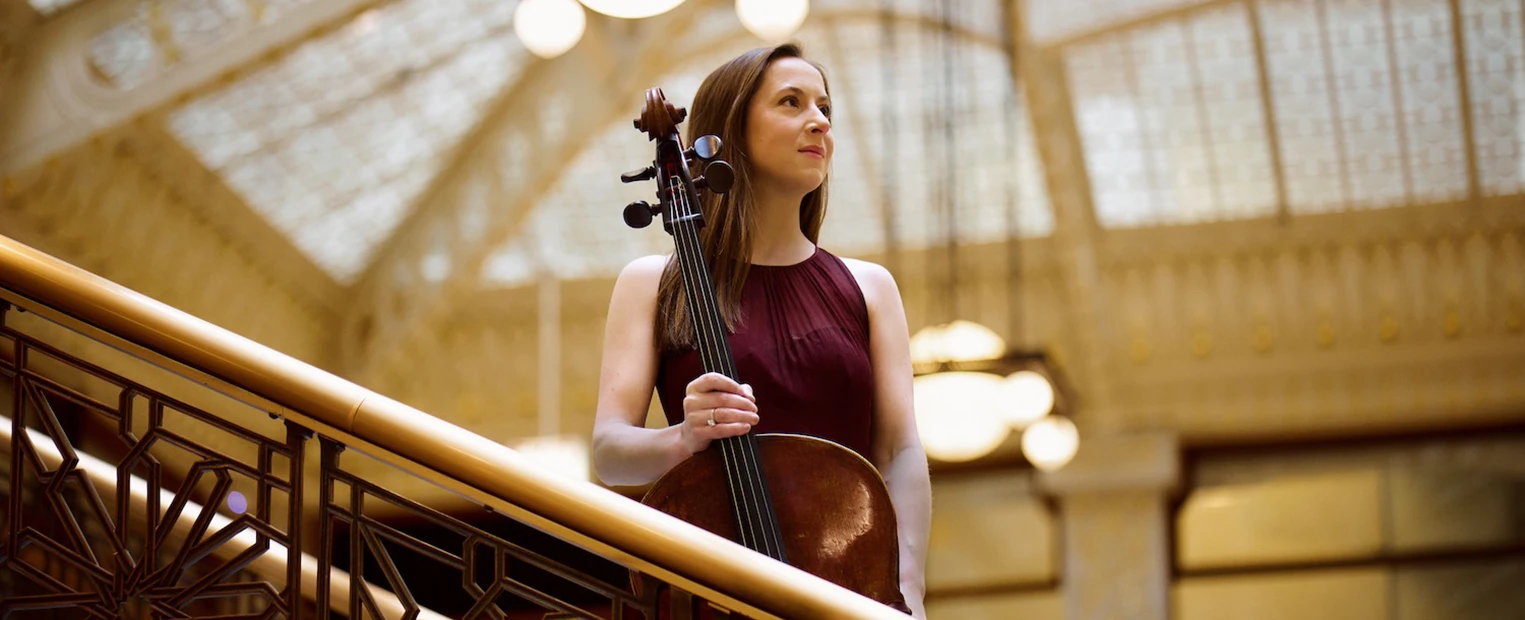Juliette Herlin, in a maroon dress, stands with her cello